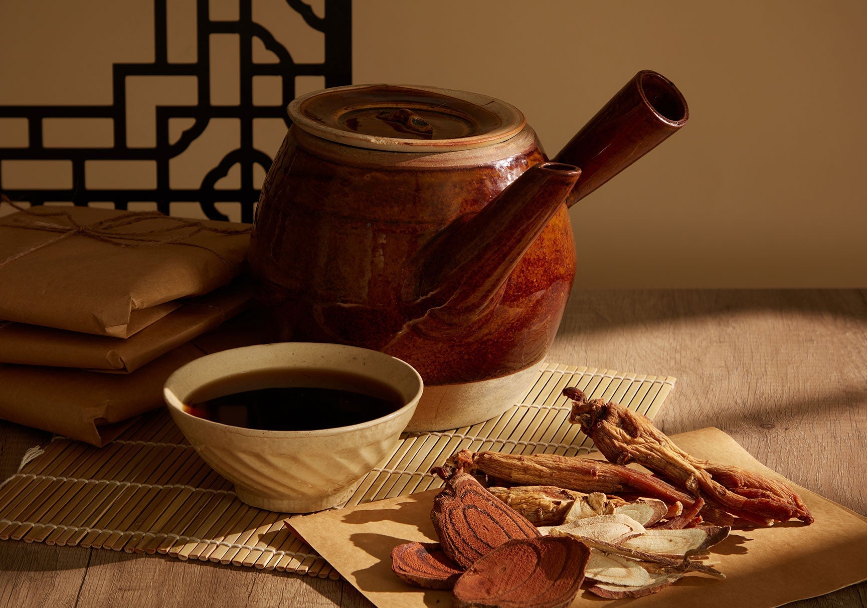 Brown teapot with two handles and a bowl of brown liquid on a table, suggesting a tea setting.