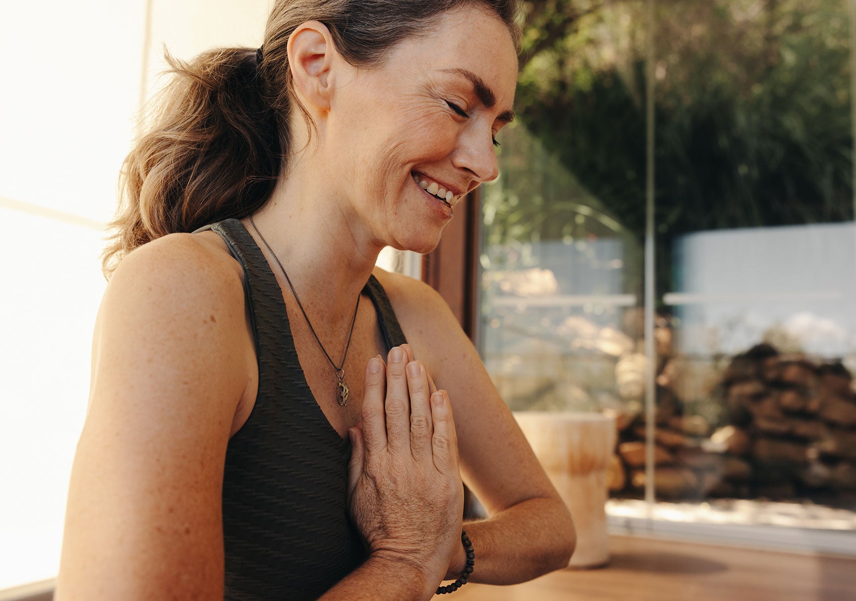 Happy senior woman smiling while meditating in prayer position at home. Mature woman doing a relaxation exercise during a yoga session. Cheerful elderly woman practicing a healthy workout routine.