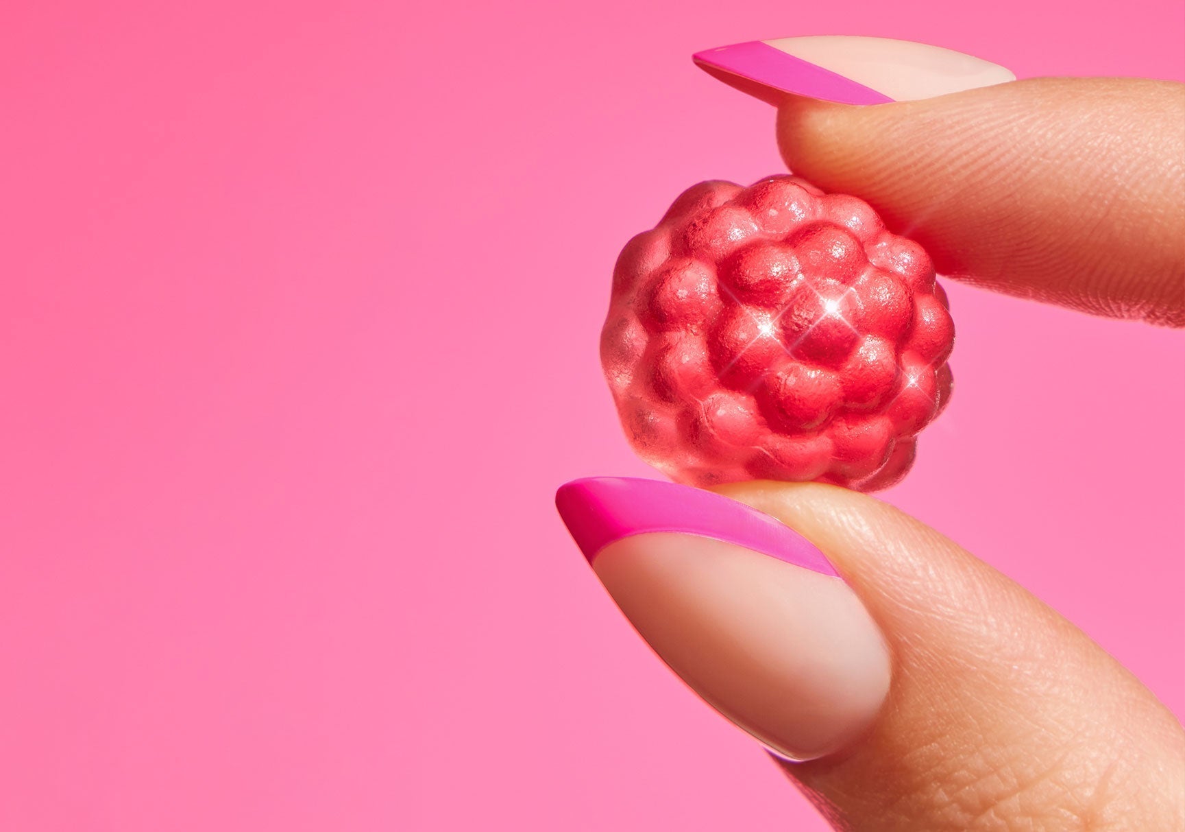 A hand holding a raspberry-shaped candy, highlighting the detailed texture and vibrant red color of the candy, with a visible fingernail.