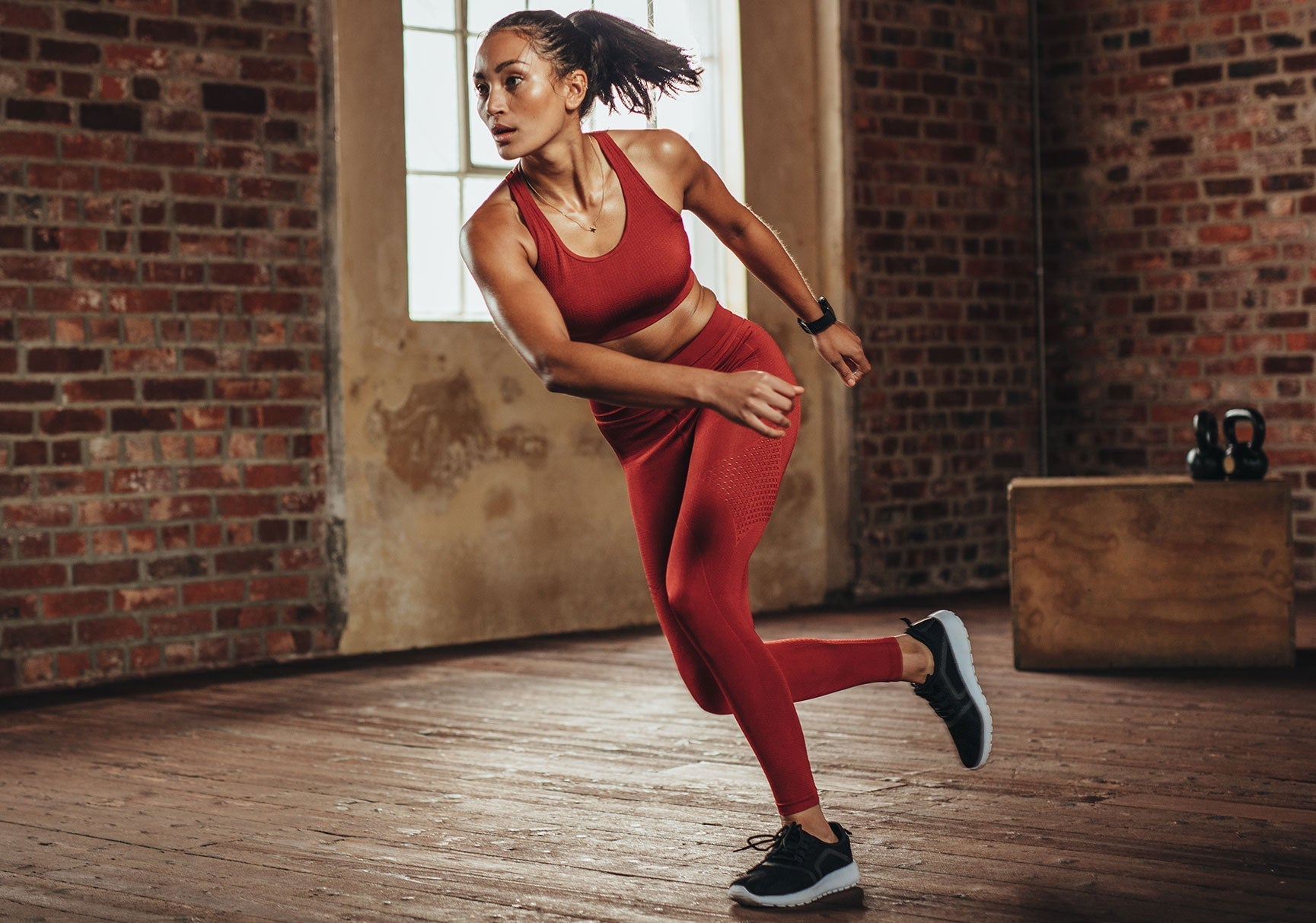 A woman in red running on a treadmill indoors, wearing black shoes, with a focus on her footwear.