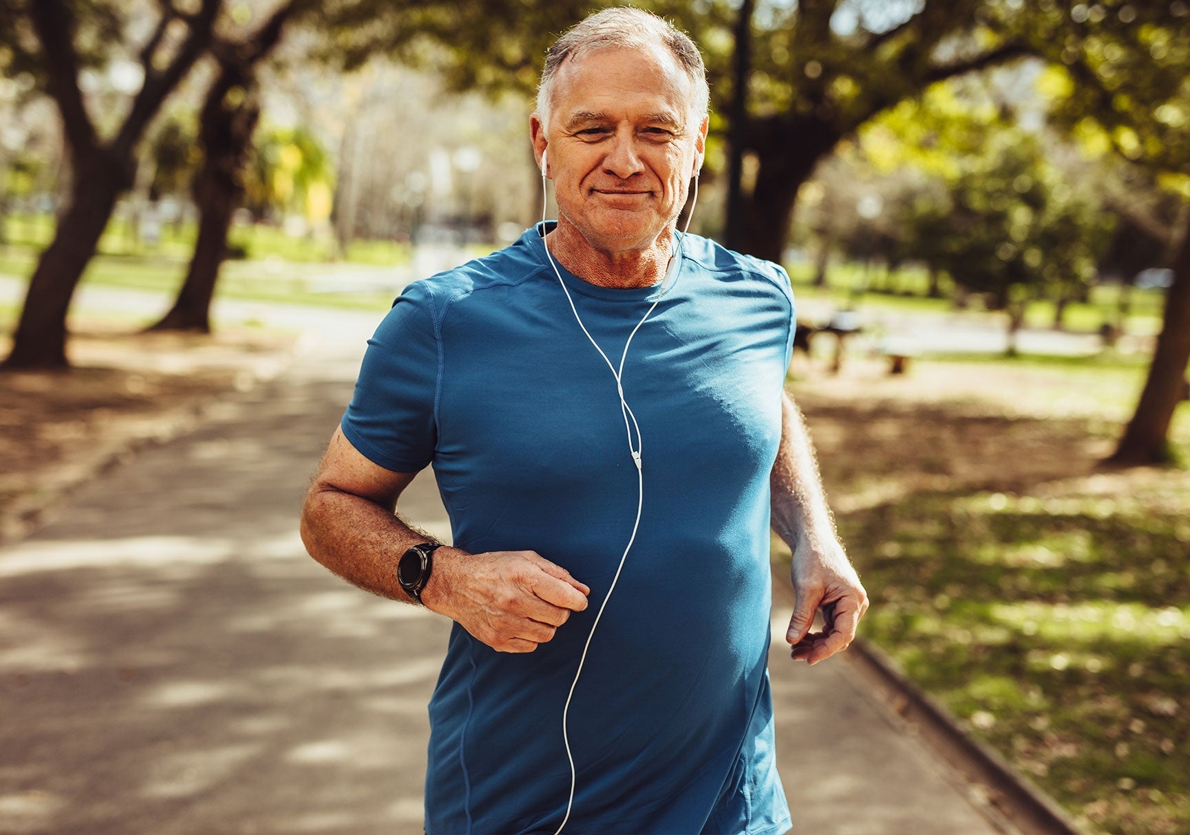 A man running in a park, wearing headphones and smiling, with a close-up of a watch on his wrist.