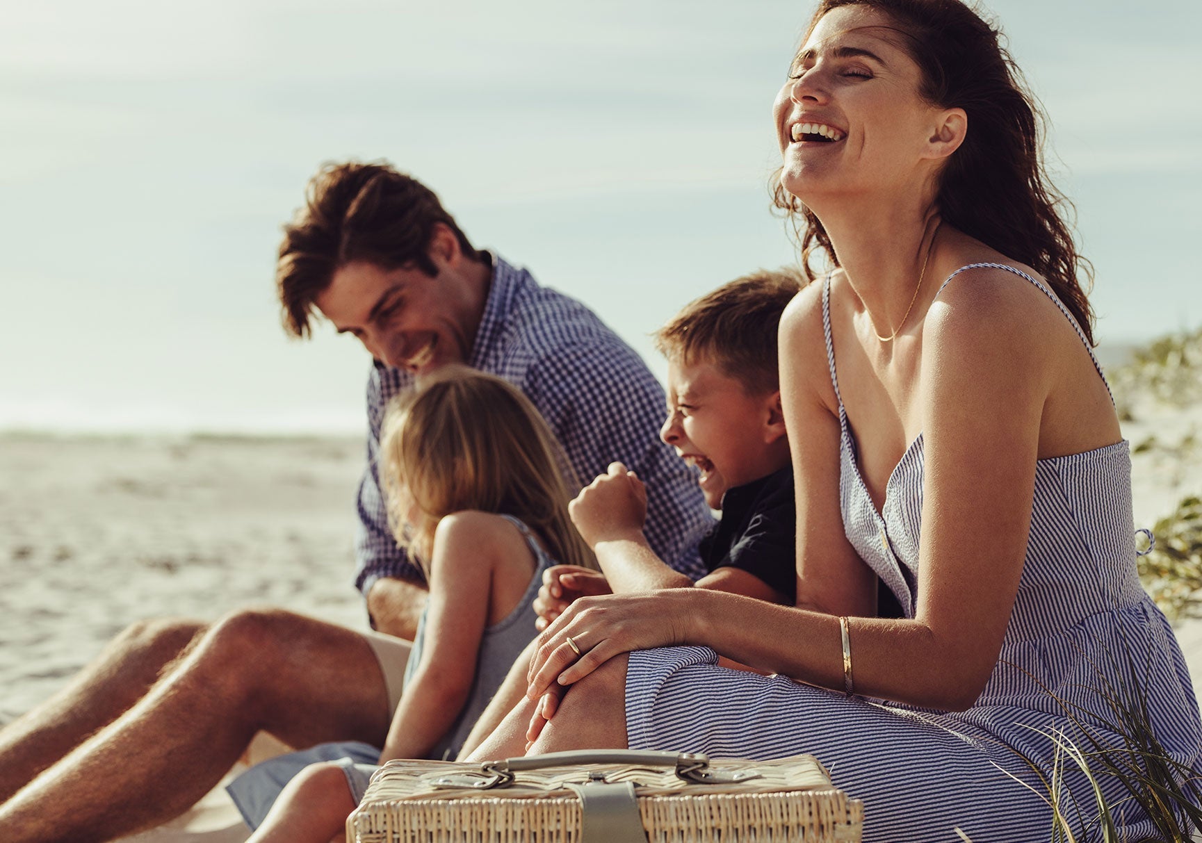 A group of people laughing and sitting on a beach, with a close-up of a basket in the foreground.