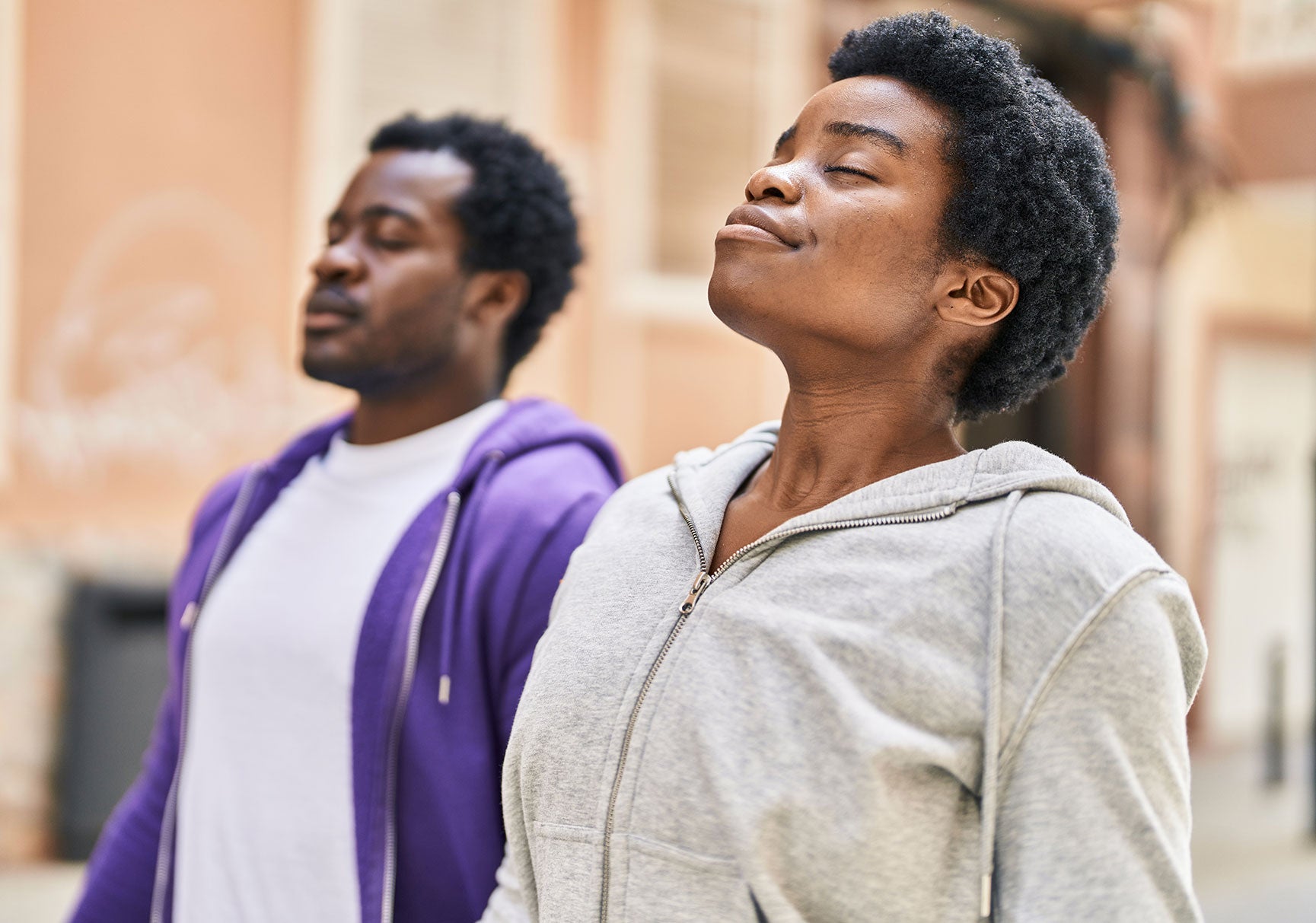 A man in a purple jacket and a woman with closed eyes stand closely together, both appearing serene and peaceful.