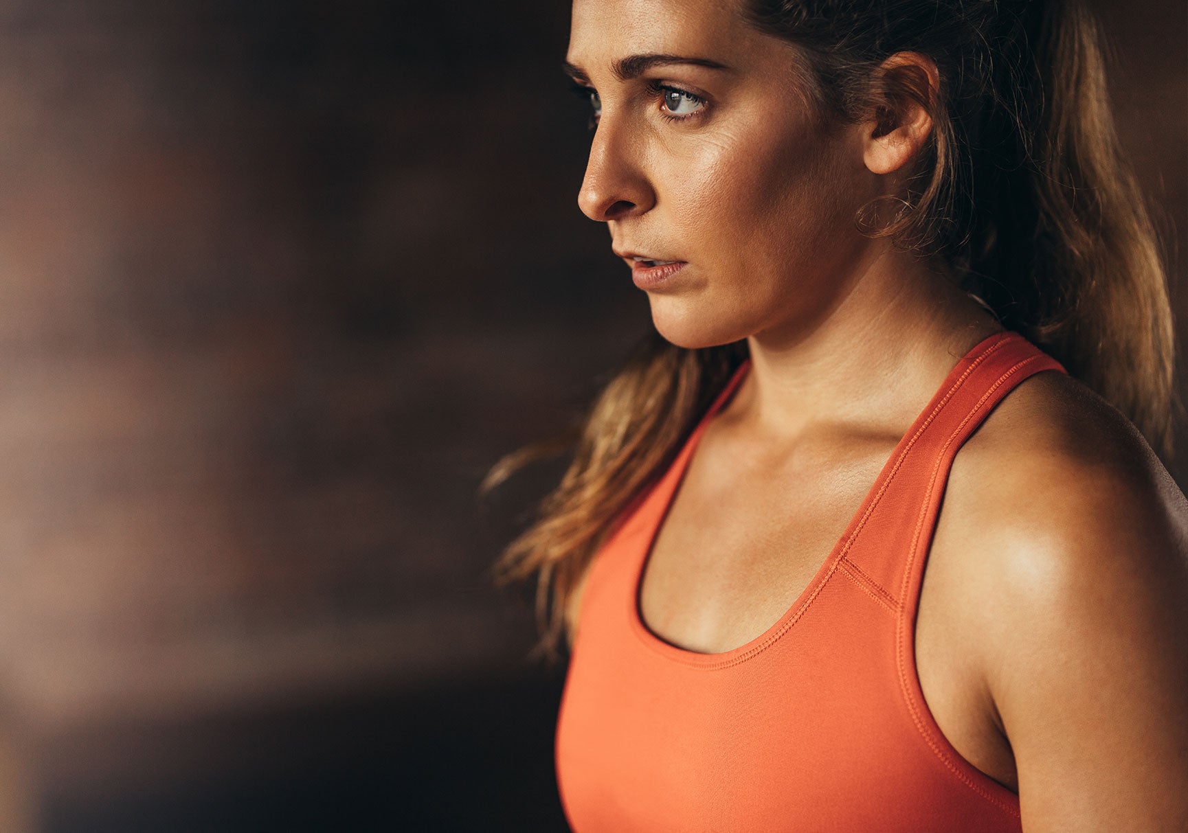 Close up of young woman in orange sports bra looking away. Female taking break after workout.