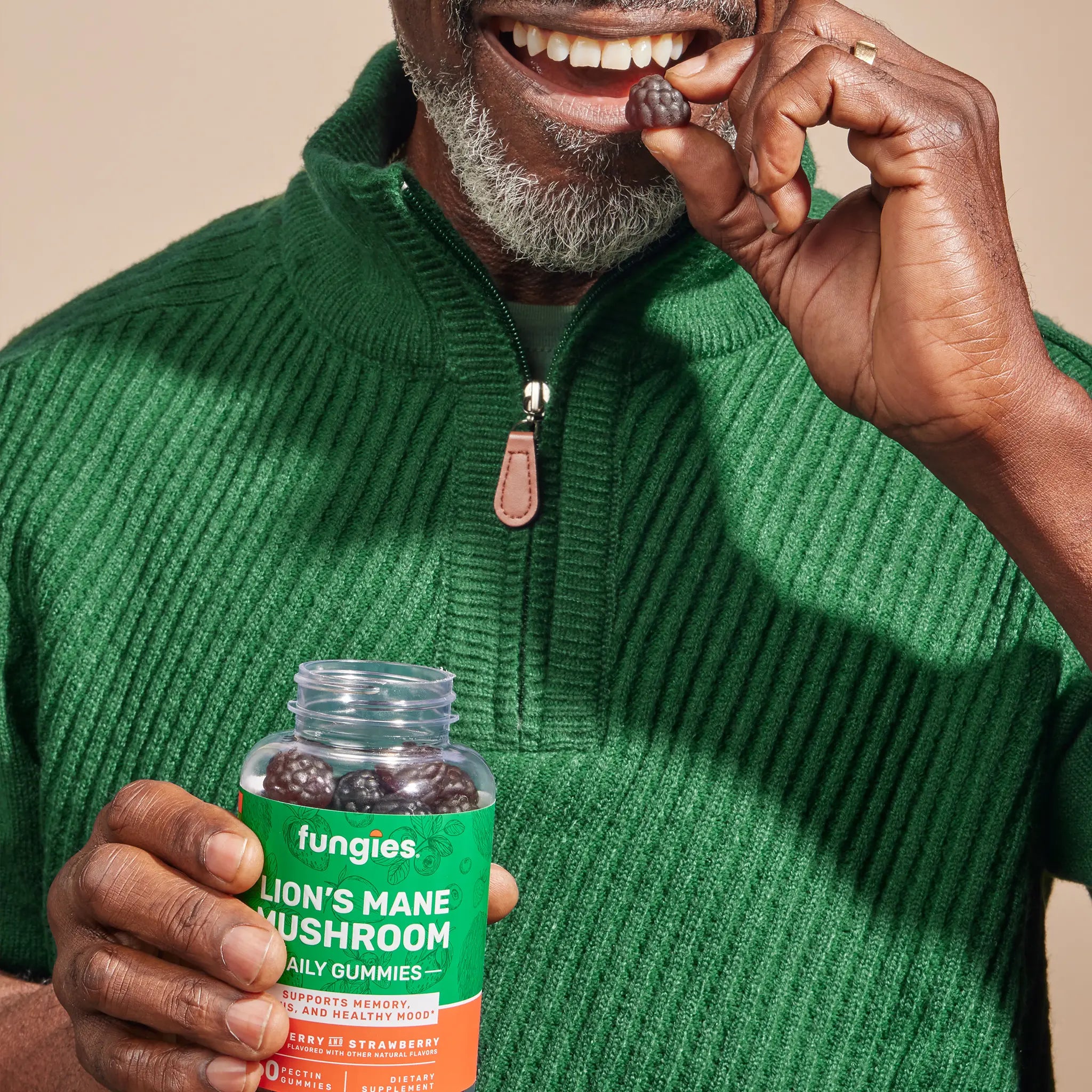 Person with green sweater holds Fungies Lion's Mane Mushroom Gummies, showing the jar and popping a berry-flavored gummy, promoting memory and focus support.
