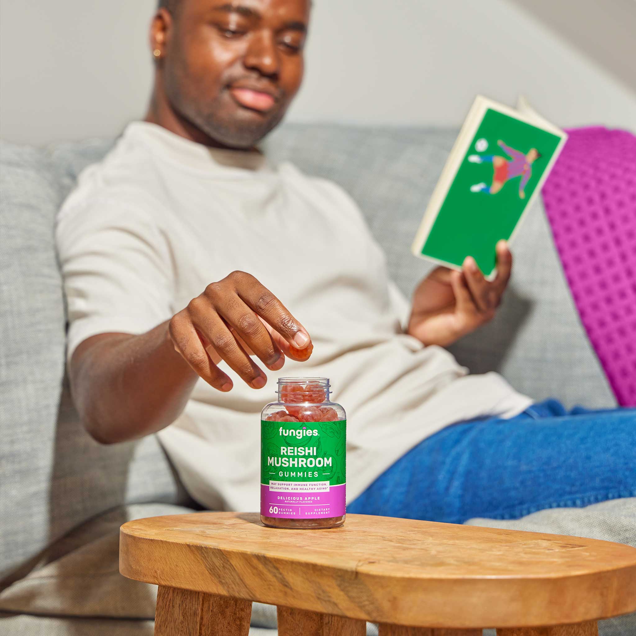 Man holding a jar of Reishi Mushroom Gummies (60 Count) on a couch, showcasing the product's focus on wellness and flavor.