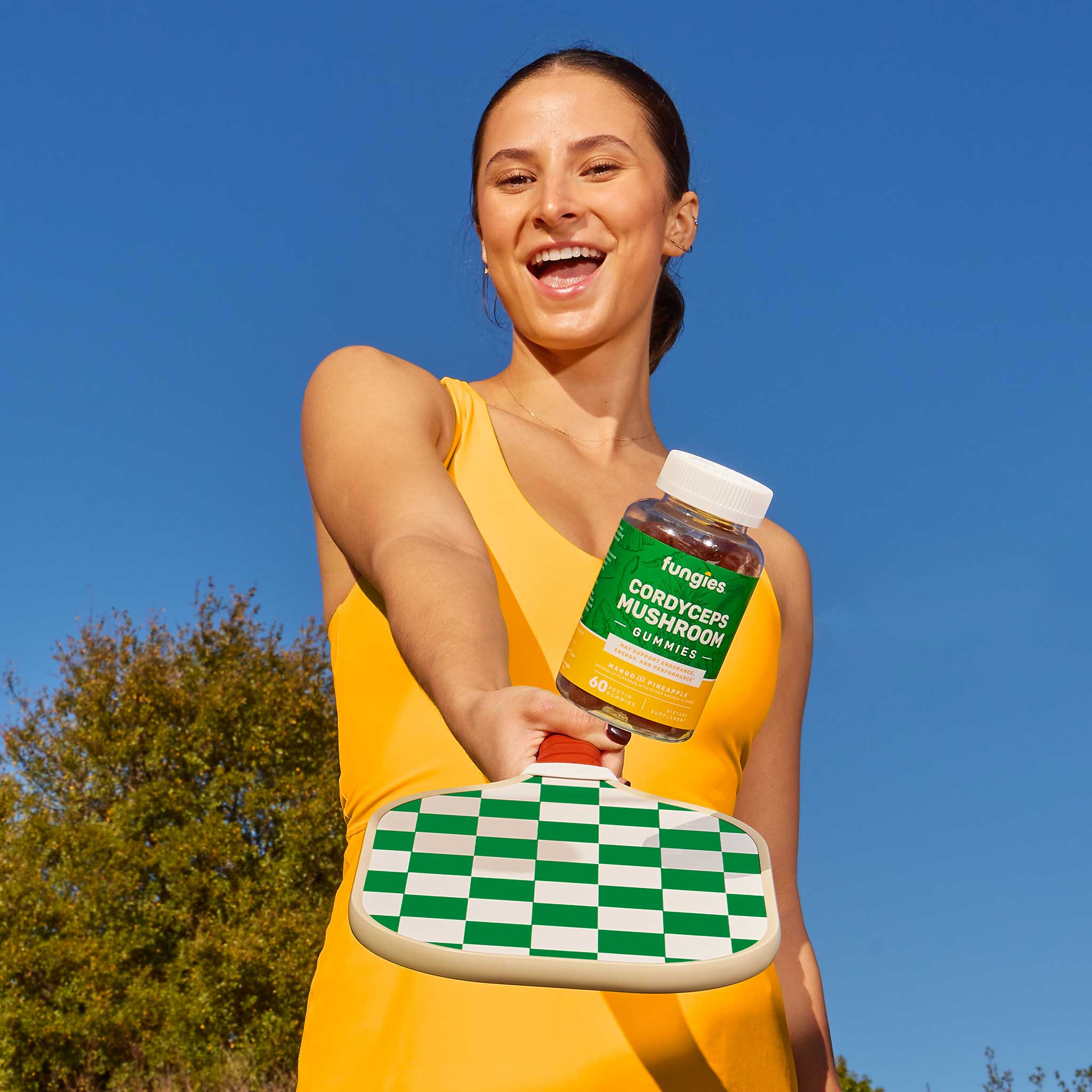 Woman smiling while holding a bottle of Cordyceps Mushroom Gummies (60 Count), highlighting its use as a natural energy-boosting supplement.